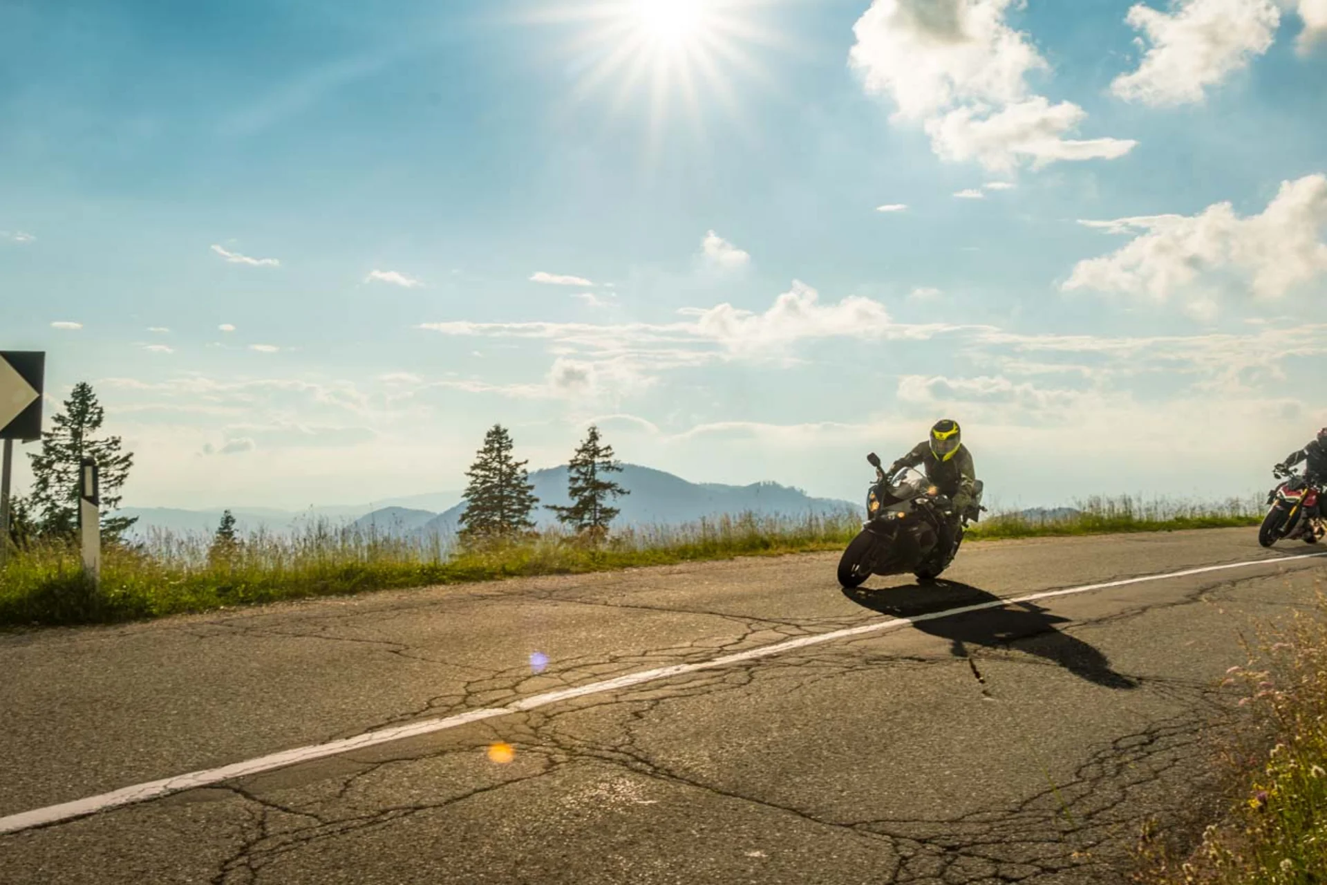 Zwei Motorräder fahren an sonnigem Tag eine kurvige Bergstraße entlang