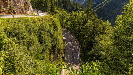 Kronkelende bergweg met motorrijder en dicht bos in de zomer