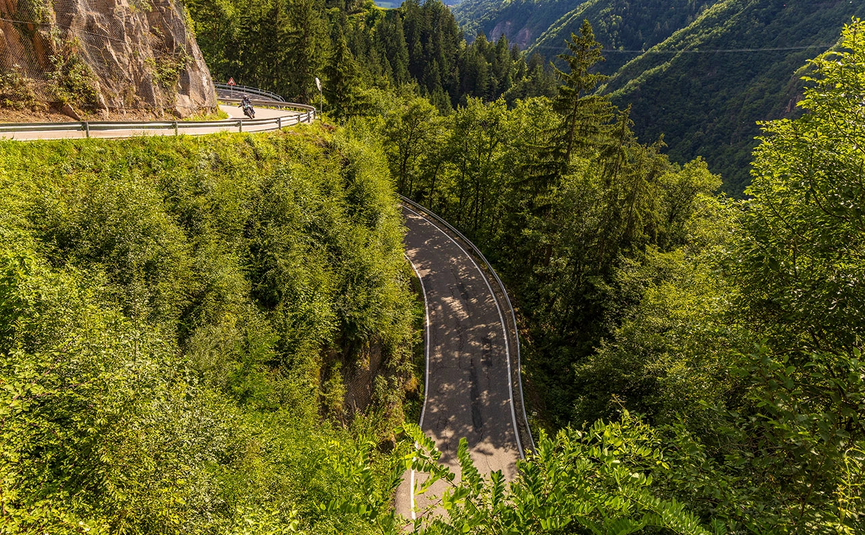 Kurvige Bergstraße mit Motorradfahrer und dichtem Wald im Sommer