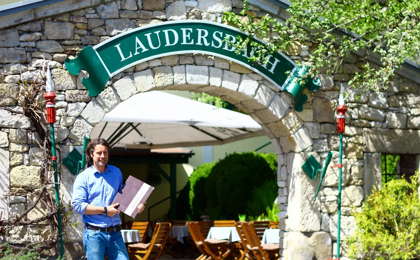 Man holding menu under stone archway with Laudersbach sign