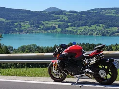 Rotes Motorrad auf Bergstraße mit See und Hügeln im Hintergrund