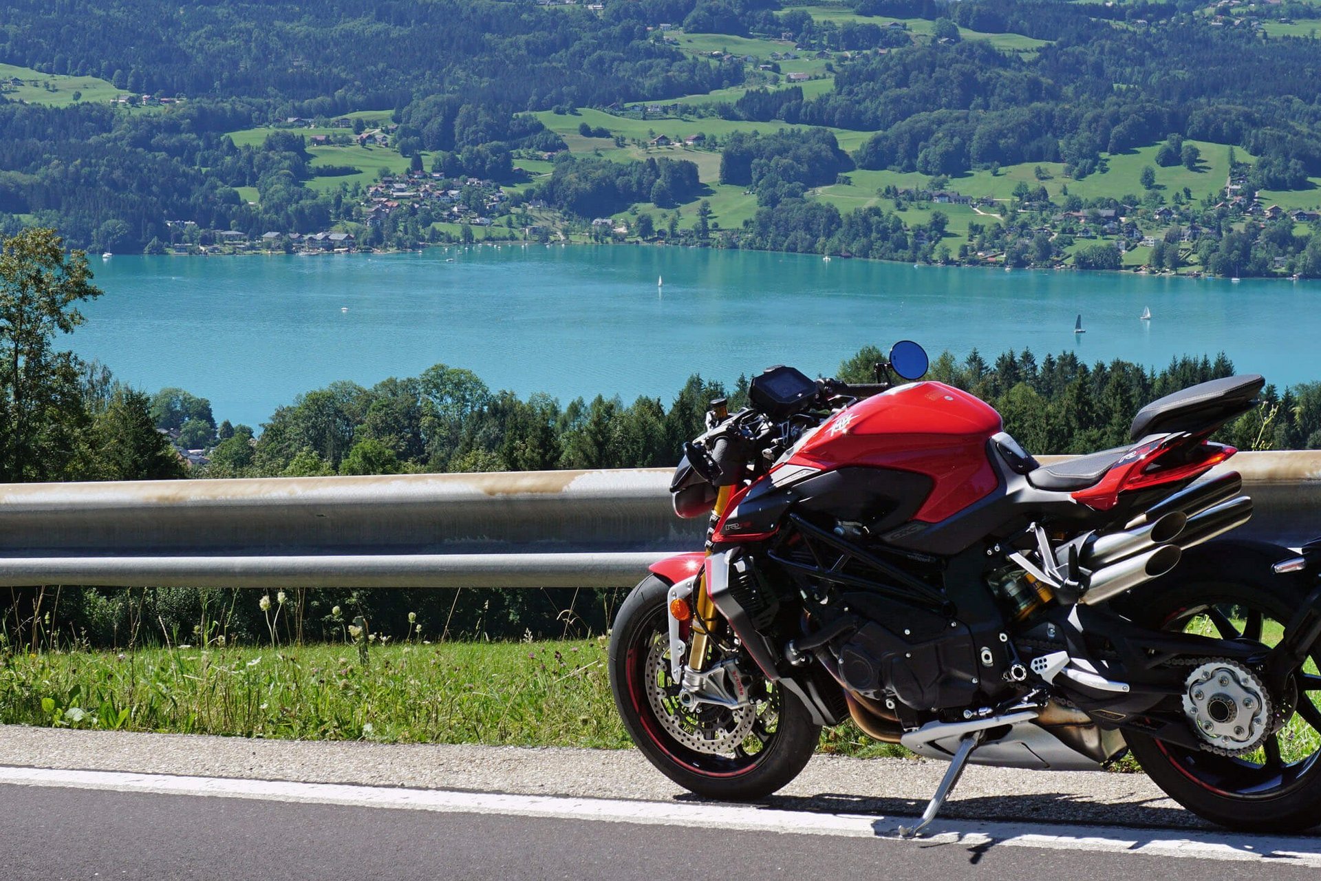 Rotes Motorrad auf Bergstraße mit See und Hügeln im Hintergrund
