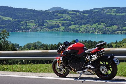 Rotes Motorrad auf Bergstraße mit See und Hügeln im Hintergrund