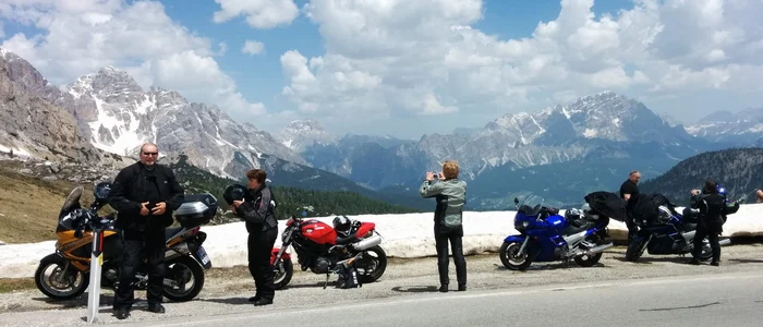 Motorcyclists stopped on mountain road with snow and clear sky