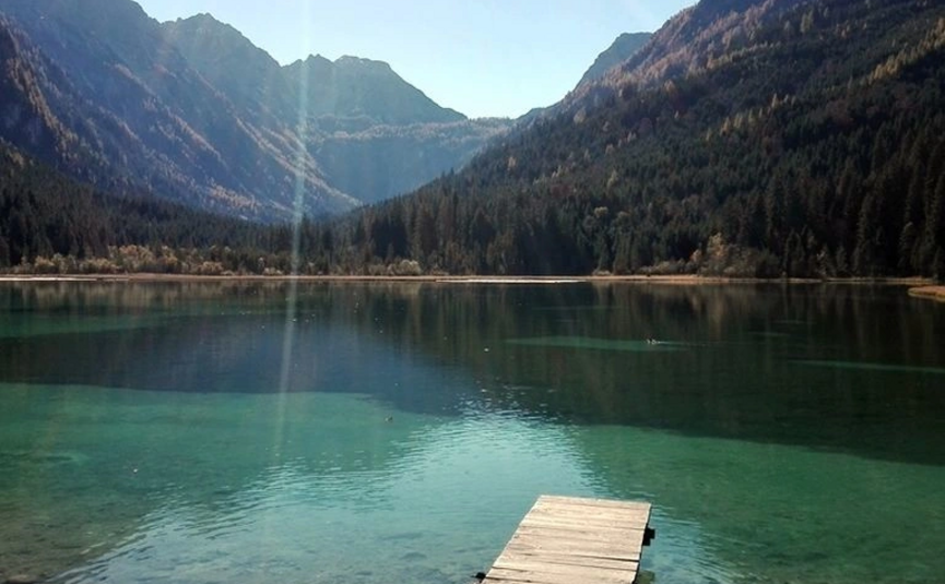 Holzsteg an klarem Bergsee mit bewaldeten Bergen im Hintergrund