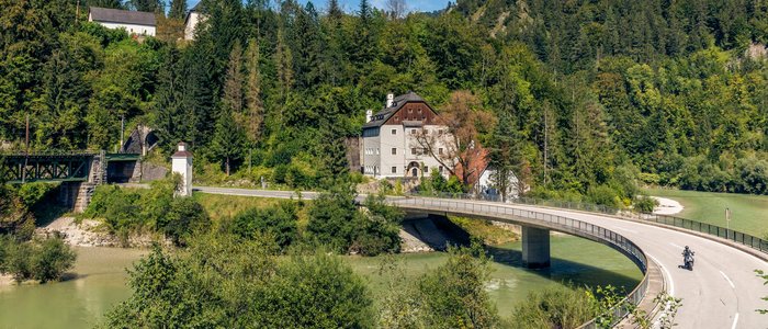 Kurvenreiche Brücke über Fluss bei Haus und Wald am sonnigen Tag