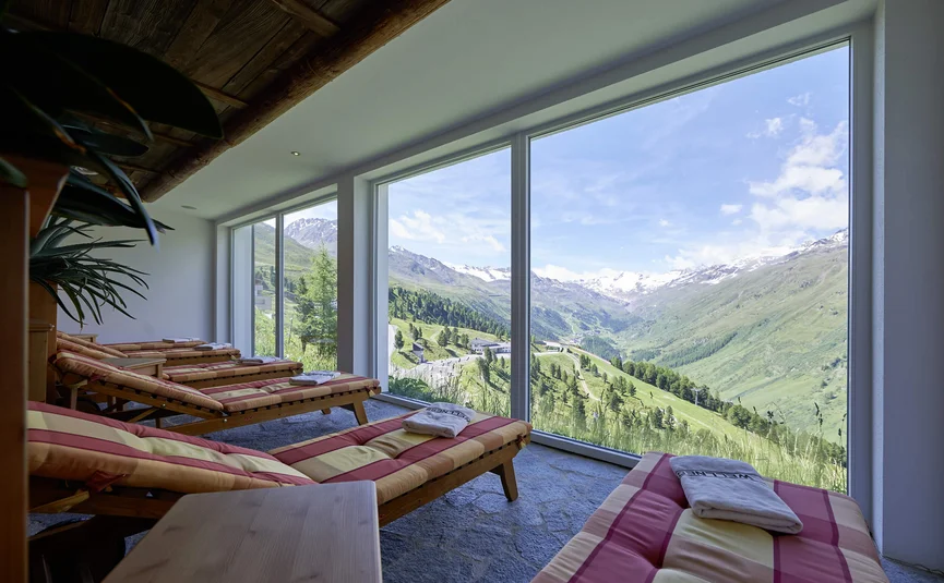 Lounge chairs by large windows overlooking green hills and snowy mountain peaks