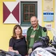 Older couple standing with motorcycle in front of yellow house with green door