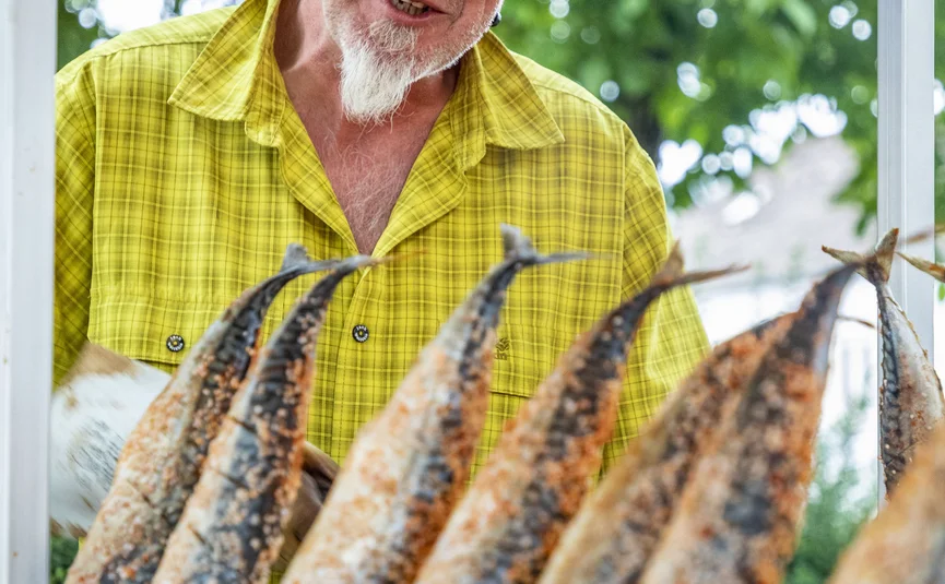 Man in yellow shirt grilling fish on skewers outdoors