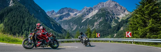 Zwei Motorräder fahren eine Kurve in den Bergen mit blauem Himmel