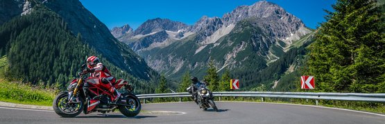 Twee motoren die een bocht in de bergen nemen bij blauwe lucht