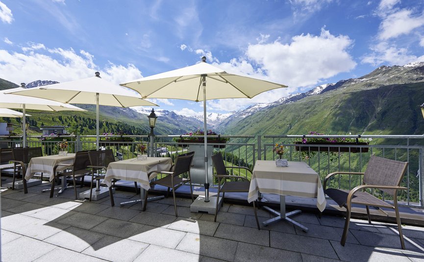 Terrasse mit Tischen und Sonnenschirmen vor Bergpanorama