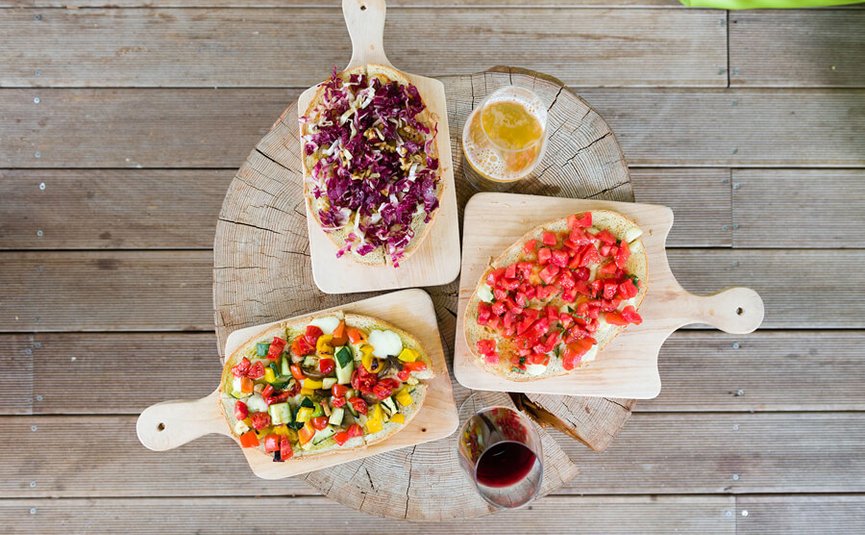 Drei belegte Brote auf Holzbrettchen mit Bier und Rotwein auf Holztisch