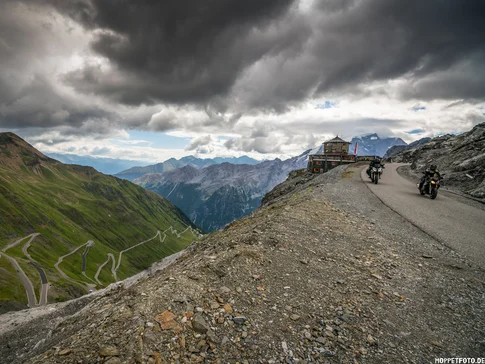 Motorradfahrer auf kurvenreicher Bergstraße mit dramatischem Himmel