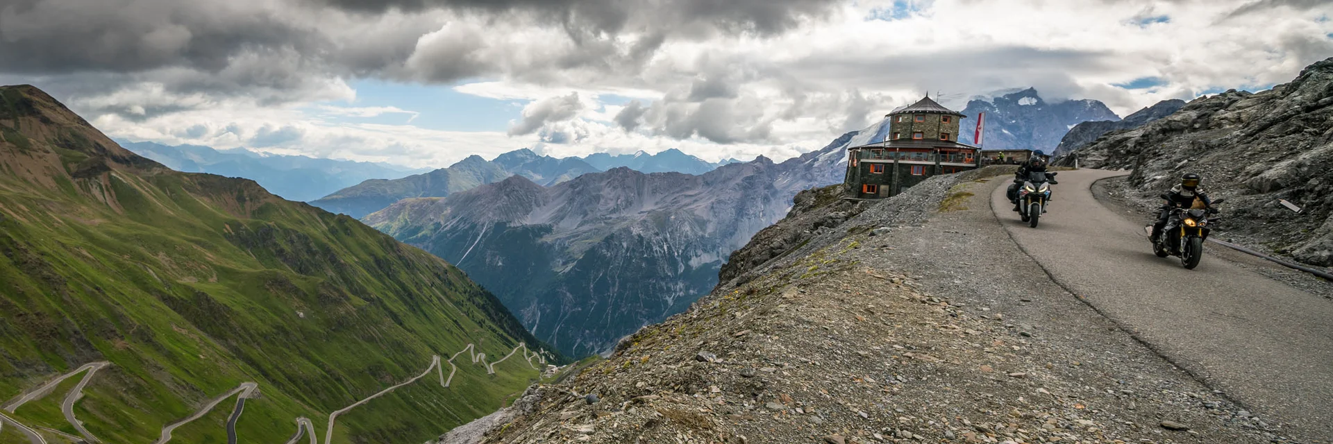 Motorcyclists on winding mountain road under dramatic cloudy sky