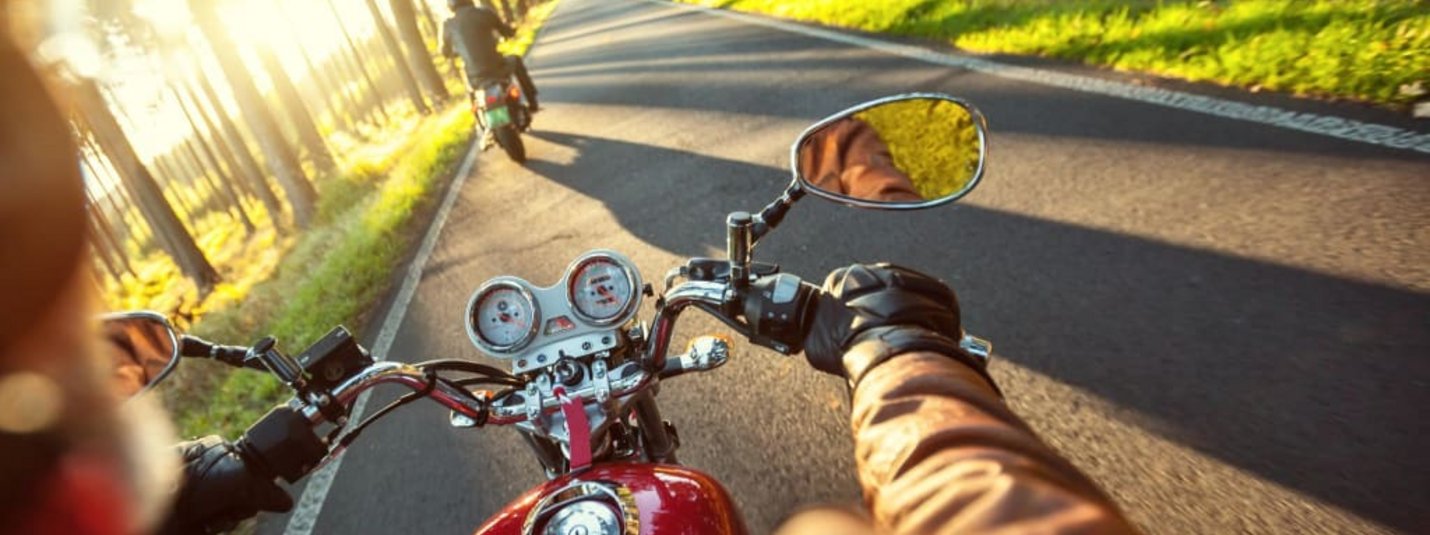 Motorradfahrer fahren auf einer sonnigen Landstraße durch einen bewaldeten Bereich