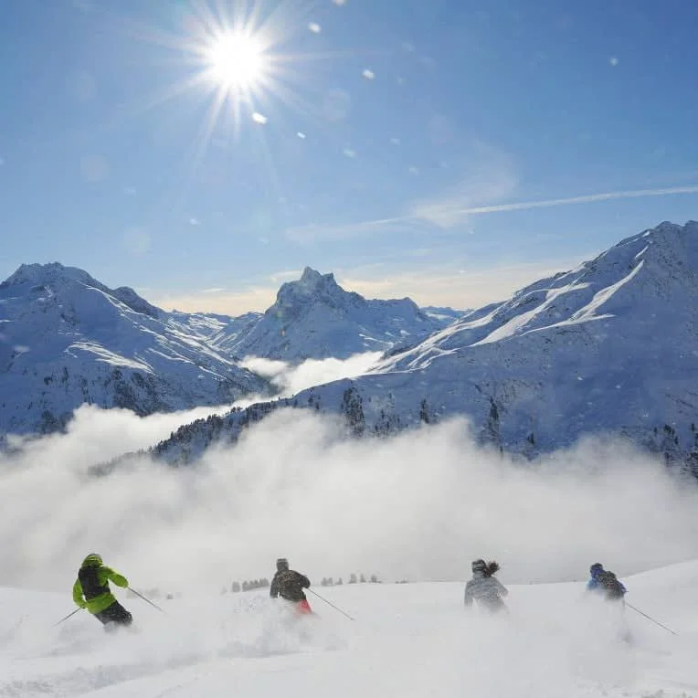 Skifahrer fahren durch tiefen Schnee vor verschneiter Berglandschaft