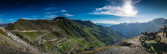 Kurvige Bergstraße mit Motorrädern und Bergpanorama bei Sonnenschein