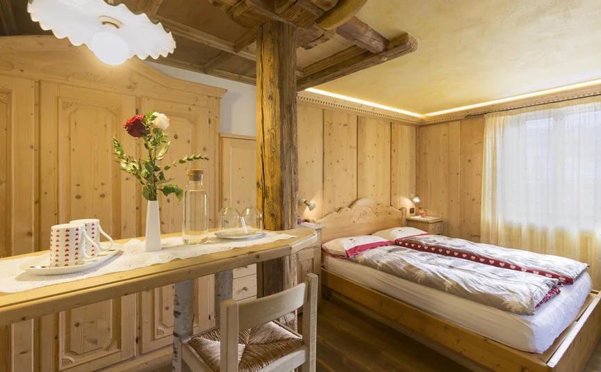 Hotel La Stüa **** © Hotel La Stüa Gemütliches Holzschlafzimmer mit Doppelbett und kleinem Tisch mit Blumen