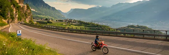 Motorradfahrer auf Bergstraße mit Aussicht auf Tal und Berge bei bewölktem Himmel
