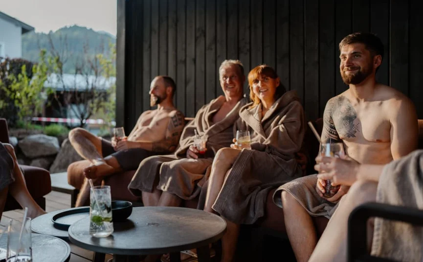 Sweaty Weekends Gruppe von Menschen entspannt in Bademänteln und mit Getränken auf Terrasse