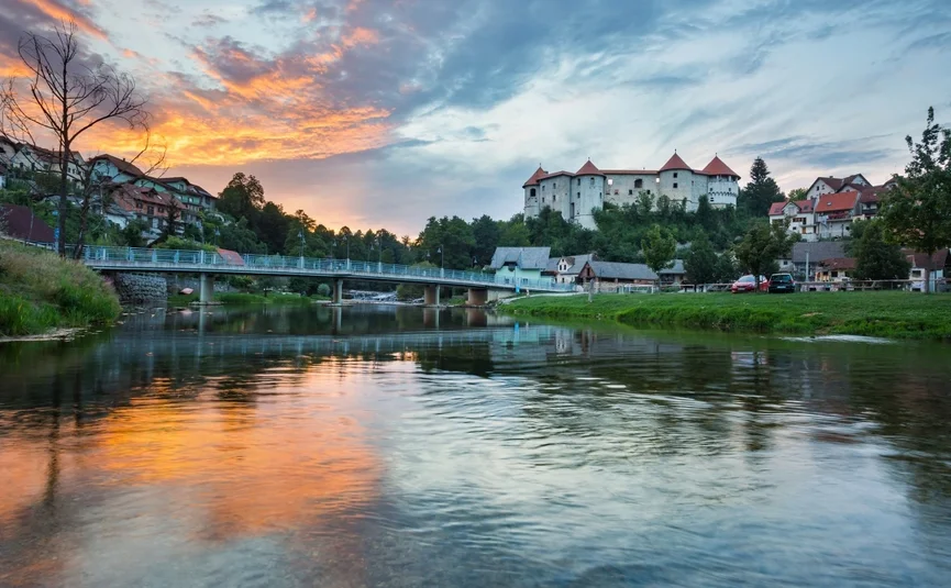 Schloss auf Hügel mit Fluss und Brücke bei Sonnenuntergang