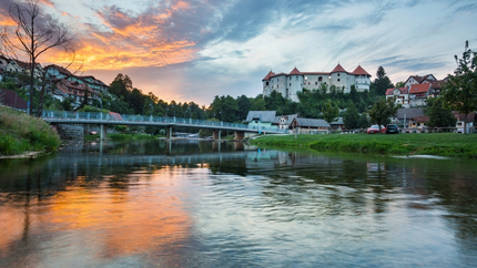 Schloss auf Hügel mit Fluss und Brücke bei Sonnenuntergang