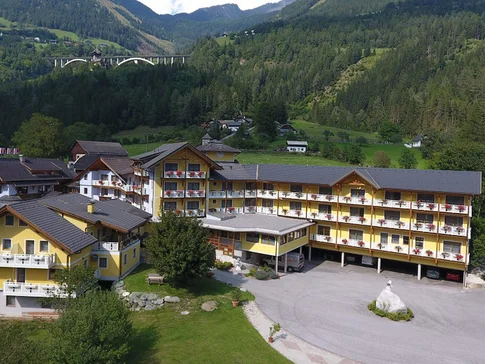 Gelbes Hotelgebäude in grüner Berglandschaft mit Autobahnbrücke im Hintergrund