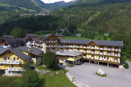 Gelbes Hotelgebäude in grüner Berglandschaft mit Autobahnbrücke im Hintergrund