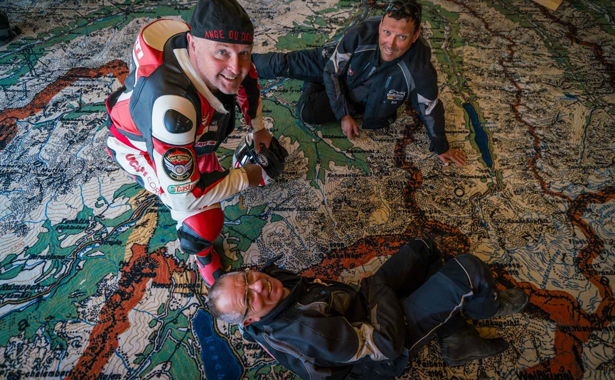 MoHo Schönauer Hof tour 13 Smugglers' tour Samnaun Three men in motorcycle gear on a large map spread on the floor