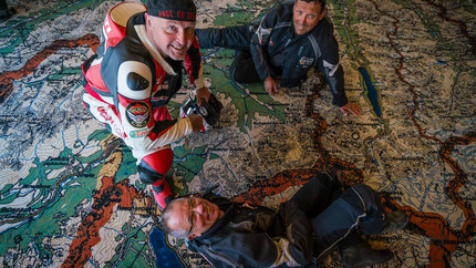 Drei Männer in Motorradkleidung auf einer großen Landkarte auf dem Boden
