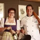 Woman holding wine bottle and man in chef coat with pan and rolling pin