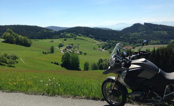 Motorcycle in front of green rolling hills with farmhouses and blue sky