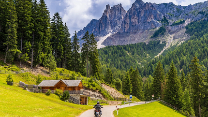 Motorcoureur op bergweg met houten huis en dennenbossen in de Alpen