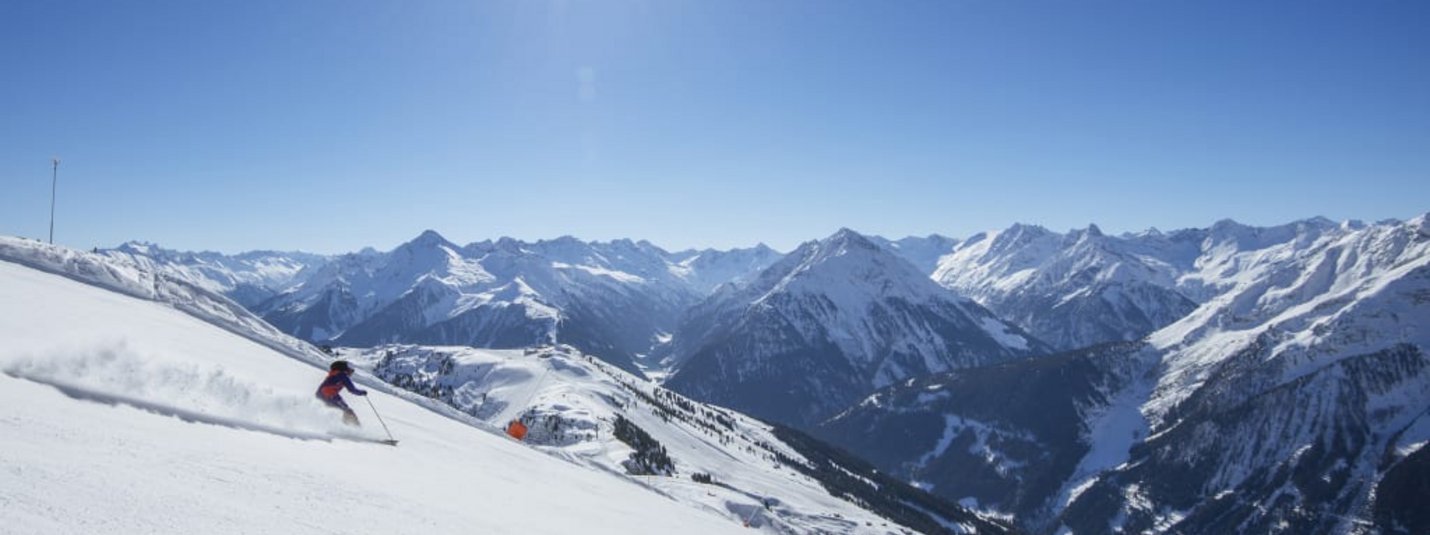 Zwei Skifahrer auf verschneitem Hang mit Bergen und strahlendem Sonnenschein