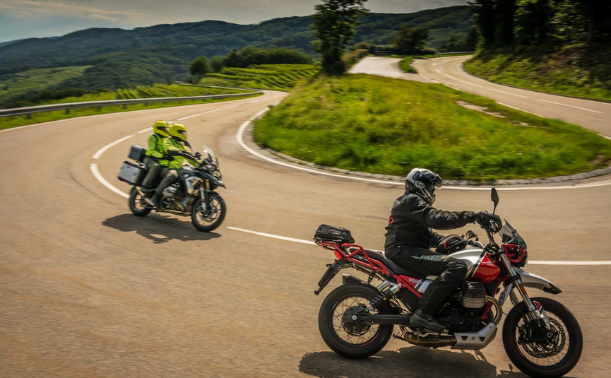 Motorradfahrer fahren auf kurviger Straße durch grüne Landschaft in den Bergen