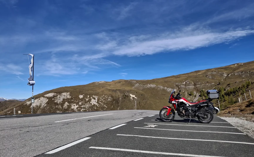 Nockalmtour der Klassiker Tour 9 Rotes Motorrad auf Parkplatz mit Berglandschaft und blauem Himmel