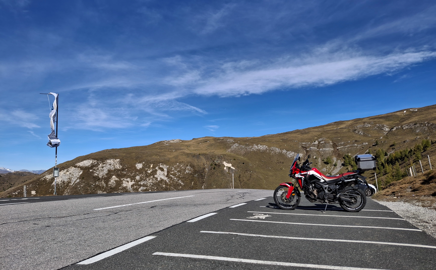 Rotes Motorrad auf Parkplatz mit Berglandschaft und blauem Himmel