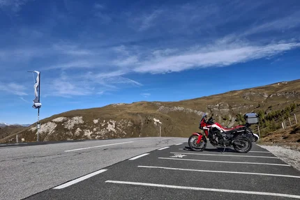 Red motorcycle parked with mountains and blue sky in the background