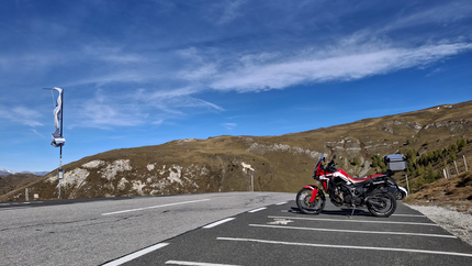 Nockalmtour der Klassiker Tour 9 Rotes Motorrad auf Parkplatz mit Berglandschaft und blauem Himmel