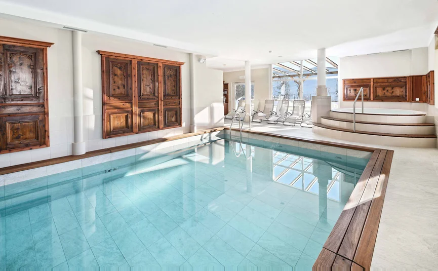 Indoor pool with clear water and a hot tub near wooden wall panels
