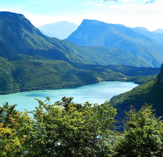 Berglandschaft mit grünem Wald und See im Tal unter blauem Himmel
