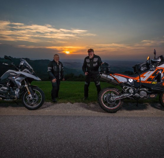 Twee mannen met motoren bij zonsondergang op een landweg