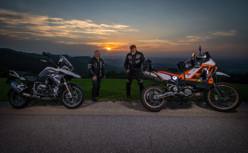 Zwei Männer mit Motorrädern bei Sonnenuntergang auf einer Landstraße