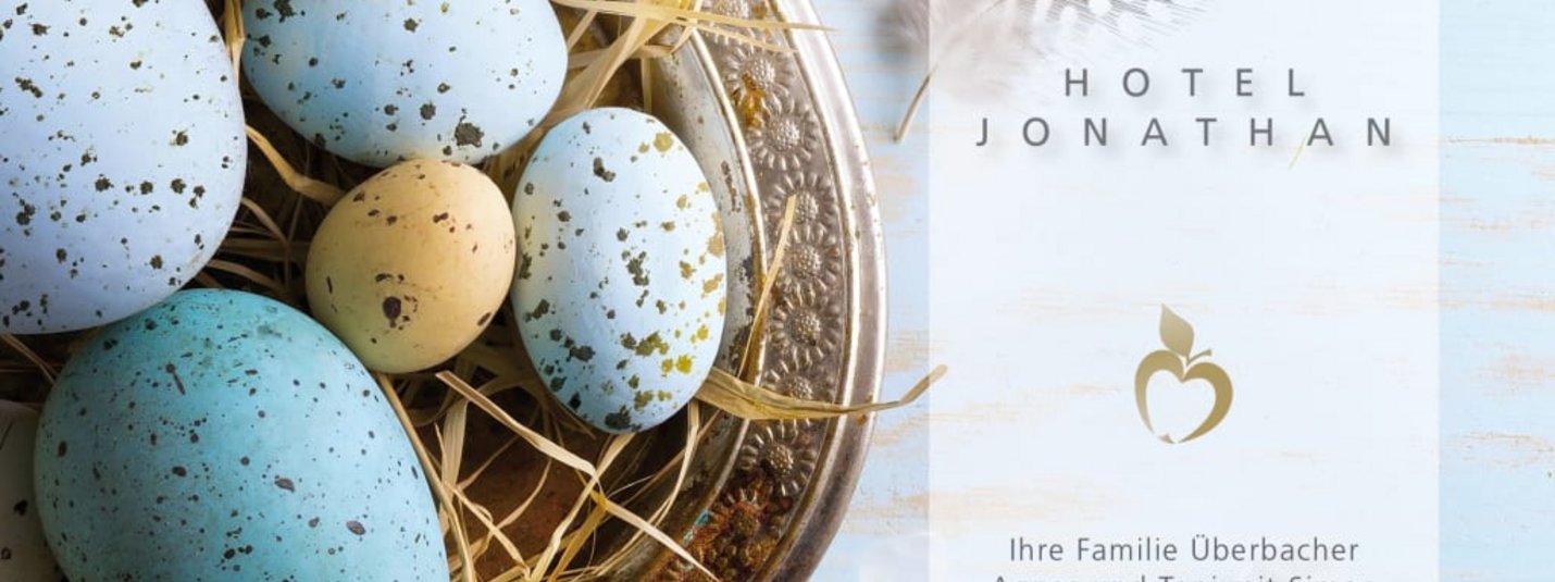 Bunte Ostereier in einer Schale mit Federn und Ostergruß