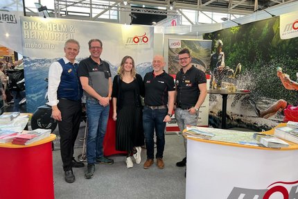 Fünf Personen stehen auf einer Motorradmesse am MOHO Motorradhotels Stand