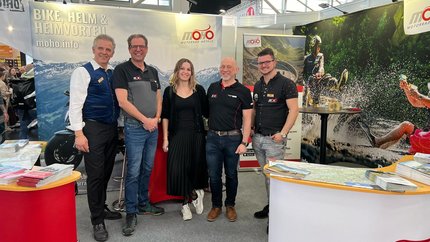 Fünf Personen stehen auf einer Motorradmesse am MOHO Motorradhotels Stand