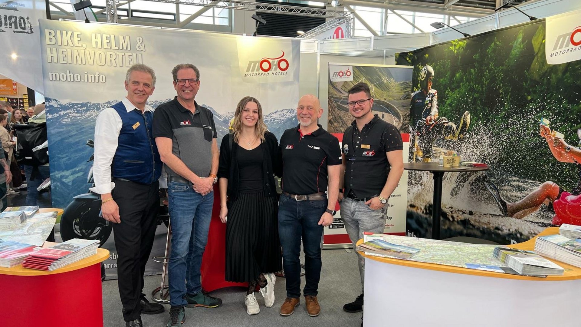 Fünf Personen stehen auf einer Motorradmesse am MOHO Motorradhotels Stand