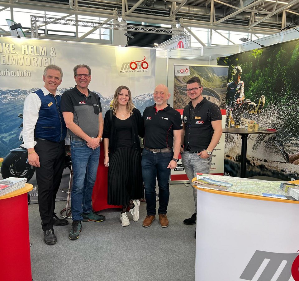 Fünf Personen stehen auf einer Motorradmesse am MOHO Motorradhotels Stand