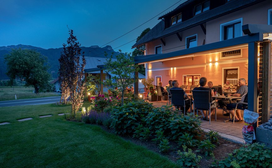 Abendliche Gartenparty mit Freunden auf einer Terrasse neben einem Haus im Grünen